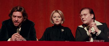 Movie still from “Deep Red” (1975), directed by Dario Argento – A woman in a black dress sitting in front of a red curtain; Medium shot, Low angle