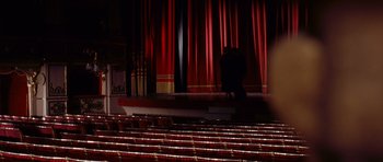 Movie still from “Deep Red” (1975), directed by Dario Argento – A person sitting on a stage in front of a red curtain; Extreme Wide shot, High angle