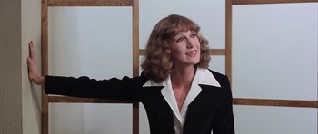 Movie still from “Deep Red” (1975), directed by Dario Argento – A woman in a black and white suit smiling for the camera; Close Up shot, Low angle
