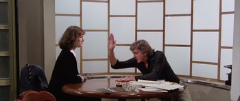 Movie still from “Deep Red” (1975), directed by Dario Argento – Two people sitting at a table with one giving a high - five; Medium shot, Over the shoulder angle