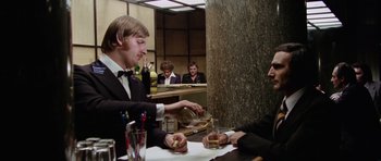 Movie still from “Deep Red” (1975), directed by Dario Argento – A man sitting at a table with a glass of whiskey; Medium shot, Over the shoulder angle
