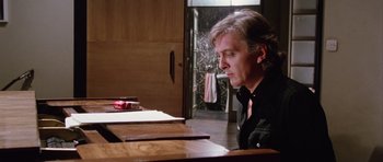 Movie still from “Deep Red” (1975), directed by Dario Argento – A man sitting at a table in front of papers; Close Up shot, Low angle