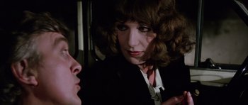 Movie still from “Deep Red” (1975), directed by Dario Argento – A woman in a black jacket and white shirt is talking to another woman; Close Up shot, Over the shoulder angle