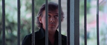 Movie still from “Deep Red” (1975), directed by Dario Argento – A man standing behind a metal fence looking at the camera; Close Up shot, Low angle