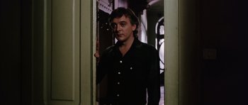 Movie still from “Deep Red” (1975), directed by Dario Argento – A man in a black shirt standing in a doorway; Medium shot, Low angle