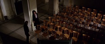 Movie still from “Deep Red” (1975), directed by Dario Argento – A woman standing in front of a room filled with chairs; Extreme Wide shot, High angle