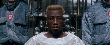 Movie still from “Demolition Man” (1993), directed by Marco Brambilla – A black man with blonde hair is sitting in front of a metal cage; Close Up shot, High angle