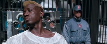 Movie still from “Demolition Man” (1993), directed by Marco Brambilla – A man in a white shirt is standing next to another man in a blue jacket; Close Up shot, Low angle