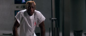 Movie still from “Demolition Man” (1993), directed by Marco Brambilla – A man in a white shirt is standing in front of a mirror; Close Up shot, Over the shoulder angle