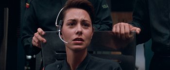 Movie still from “Demolition Man” (1993), directed by Marco Brambilla – A woman sitting on top of a bench with a headset on; Close Up shot, Over the shoulder angle