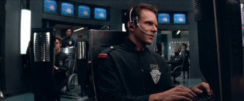 Movie still from “Demolition Man” (1993), directed by Marco Brambilla – A man in a uniform sitting in a chair with a headset on; Medium shot, Over the shoulder angle