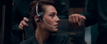 Movie still from “Demolition Man” (1993), directed by Marco Brambilla – A woman with a headset on sitting on a bench; Close Up shot, Over the shoulder angle