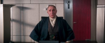 Movie still from “Demolition Man” (1993), directed by Marco Brambilla – An older man wearing a robe sitting in a chair; Medium shot, Low angle
