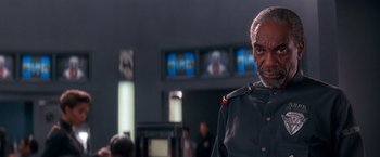 Movie still from “Demolition Man” (1993), directed by Marco Brambilla – An older man wearing a uniform in front of a television; Medium shot, Low angle