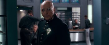 Movie still from “Demolition Man” (1993), directed by Marco Brambilla – An older man wearing a black jacket and glasses; Close Up shot, Over the shoulder angle