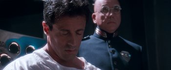 Movie still from “Demolition Man” (1993), directed by Marco Brambilla – A man in a white shirt and a man in a blue uniform; Close Up shot, Over the shoulder angle