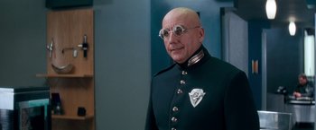 Movie still from “Demolition Man” (1993), directed by Marco Brambilla – A bald man in a uniform with round glasses; Close Up shot, Low angle