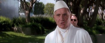Movie still from “Demolition Man” (1993), directed by Marco Brambilla – An older man wearing a white robe and a white hat; Close Up shot, Low angle