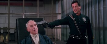 Movie still from “Demolition Man” (1993), directed by Marco Brambilla – A man holding a gun up to a man's head; Medium shot, Over the shoulder angle
