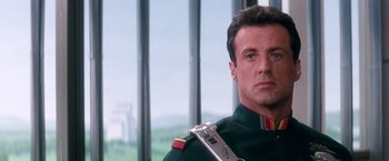 Movie still from “Demolition Man” (1993), directed by Marco Brambilla – A man in a military uniform with a machine gun in his hand; Close Up shot, Low angle