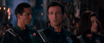 Movie still from “Demolition Man” (1993), directed by Marco Brambilla – A person wearing a uniform holding a guitar; Close Up shot, Over the shoulder angle