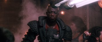 Movie still from “Demolition Man” (1993), directed by Marco Brambilla – A man in a black jacket and red shirt is looking at the camera; Close Up shot, Low angle