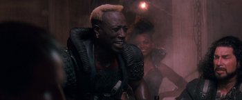 Movie still from “Demolition Man” (1993), directed by Marco Brambilla – A man in a leather jacket is standing next to a woman in a black dress; Close Up shot, Low angle