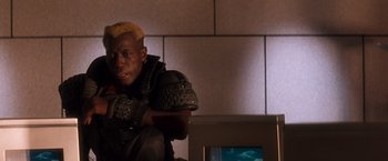 Movie still from “Demolition Man” (1993), directed by Marco Brambilla – A man sitting in front of a tv in front of a wall; Close Up shot, Low angle