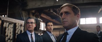 Movie still from “Ford v Ferrari” (2019), directed by James Mangold – A group of men standing next to each other in suits; Medium shot, Over the shoulder angle