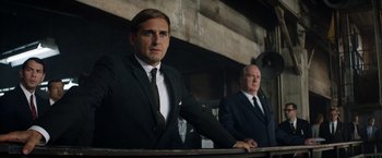 Movie still from “Ford v Ferrari” (2019), directed by James Mangold – A man in a suit and tie standing next to another man in a suit and tie; Medium shot, Low angle