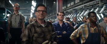 Movie still from “Ford v Ferrari” (2019), directed by James Mangold – A man standing next to another man in front of a group of people; Medium shot, Low angle