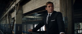 Movie still from “Ford v Ferrari” (2019), directed by James Mangold – A man in a suit and tie leaning against a railing; Medium shot, Low angle