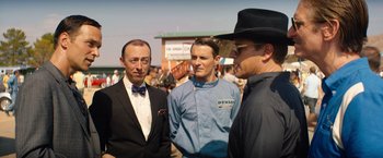 Movie still from “Ford v Ferrari” (2019), directed by James Mangold – A group of men standing next to each other on a field; Medium shot, Over the shoulder angle