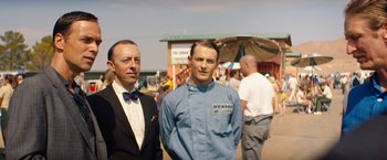 Movie still from “Ford v Ferrari” (2019), directed by James Mangold – Two men standing next to each other in front of a crowd of onlookers; Medium shot, Low angle