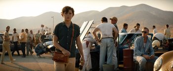 Movie still from “Ford v Ferrari” (2019), directed by James Mangold – A young man holding a purse while standing next to other men; Medium shot, Low angle