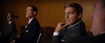 Movie still from “Ford v Ferrari” (2019), directed by James Mangold – A man in a suit and tie sitting next to another man in a suit and tie; Close Up shot, Over the shoulder angle