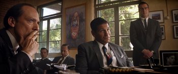 Movie still from “Ford v Ferrari” (2019), directed by James Mangold – A man in a suit and tie sitting in front of a window; Medium shot, Over the shoulder angle
