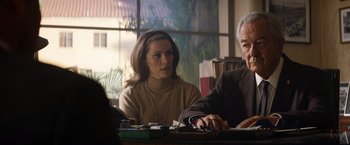 Movie still from “Ford v Ferrari” (2019), directed by James Mangold – A woman sitting next to an older man at a table; Medium shot, Over the shoulder angle