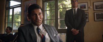 Movie still from “Ford v Ferrari” (2019), directed by James Mangold – A man in a suit and tie sitting in front of a window; Medium shot, Over the shoulder angle