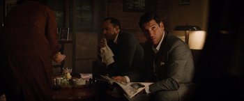 Movie still from “Ford v Ferrari” (2019), directed by James Mangold – A couple of men sitting next to each other holding papers; Medium shot, Over the shoulder angle