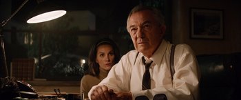 Movie still from “Ford v Ferrari” (2019), directed by James Mangold – An older man and a younger woman sitting at a table; Medium shot, Over the shoulder angle