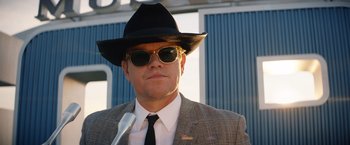 Movie still from “Ford v Ferrari” (2019), directed by James Mangold – A man in a suit and hat with a microphone; Close Up shot, Low angle