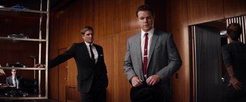 Movie still from “Ford v Ferrari” (2019), directed by James Mangold – A man in a suit and tie standing next to another man in a suit and tie; Medium shot, Low angle