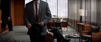Movie still from “Ford v Ferrari” (2019), directed by James Mangold – A man in a suit and tie holding a hat; Medium shot, Over the shoulder angle