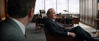 Movie still from “Ford v Ferrari” (2019), directed by James Mangold – A man sitting in a chair in front of another man in a suit; Medium shot, Over the shoulder angle