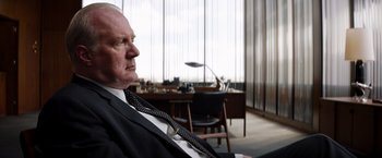 Movie still from “Ford v Ferrari” (2019), directed by James Mangold – An older man sitting in a chair in front of a desk in an office setting; Close Up shot, Over the shoulder angle