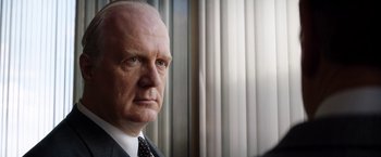 Movie still from “Ford v Ferrari” (2019), directed by James Mangold – An older man in a suit and tie looking into the distance; Close Up shot, Over the shoulder angle