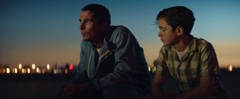 Movie still from “Ford v Ferrari” (2019), directed by James Mangold – A man sitting next to a boy on a beach; Medium shot, Low angle