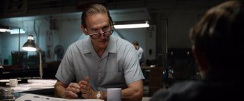 Movie still from “Ford v Ferrari” (2019), directed by James Mangold – A man sitting at a table with a cup in front of him; Close Up shot, Over the shoulder angle