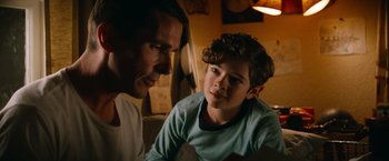 Movie still from “Ford v Ferrari” (2019), directed by James Mangold – A man and a boy sitting on a couch looking intently at each other; Close Up shot, Over the shoulder angle